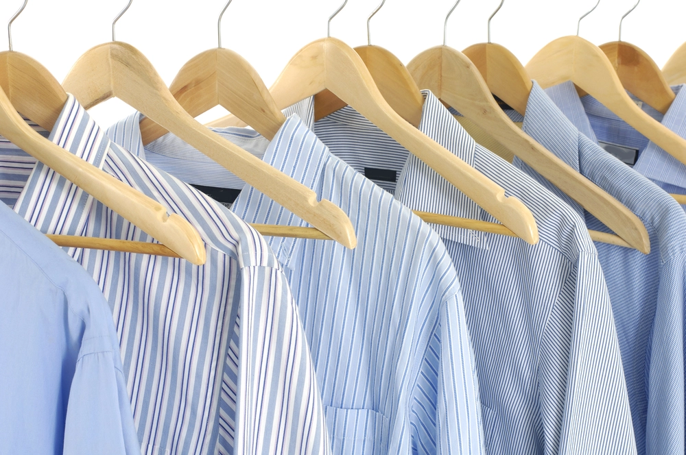 A row of blue and white striped and solid shirts hanging on wooden hangers in a closet.