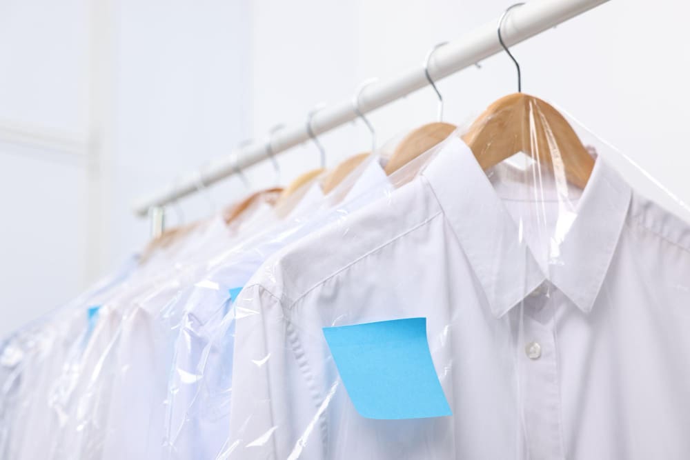 Several white dress shirts on wooden hangers, covered in clear plastic garment bags, with blue sticky notes attached to the shoulders.