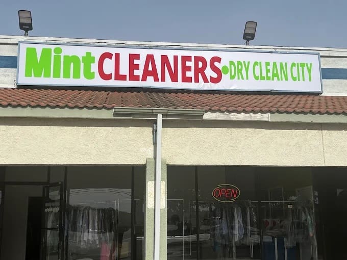 A storefront with a sign reading "Mint CLEANERS • DRY CLEAN CITY" above a dry cleaning business; an "open" sign is visible in the window.