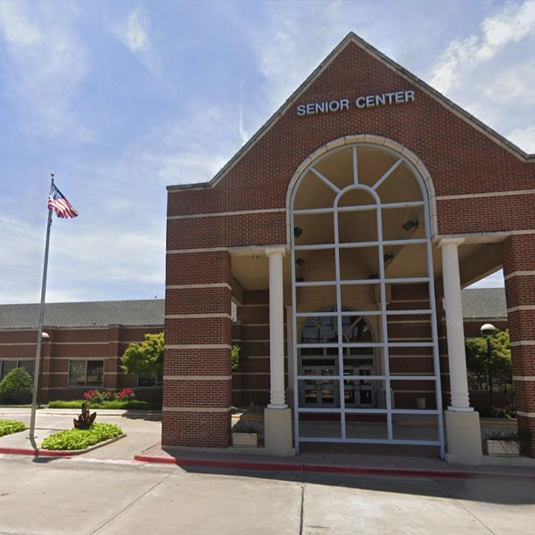 A brick building labeled "Senior Center" with large arch windows and an American flag in front under a partly cloudy sky.