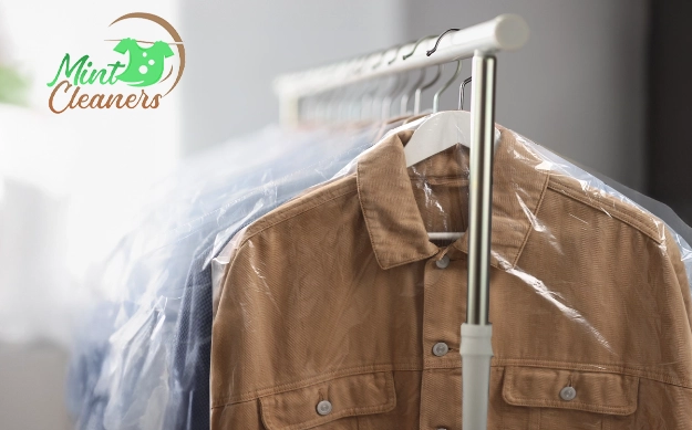 A beige shirt on a hanger covered with plastic garment bag hangs on a clothing rack; Mint Cleaners logo is visible in the corner.