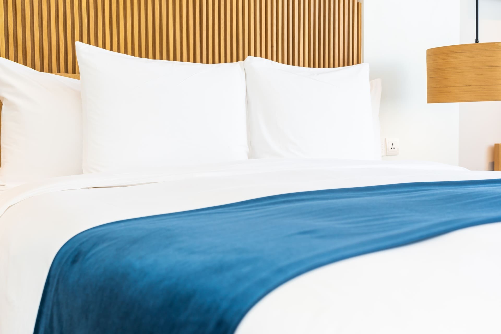 A neatly made bed with white linens, two large pillows, a wooden headboard, and a blue blanket across the foot of the bed.