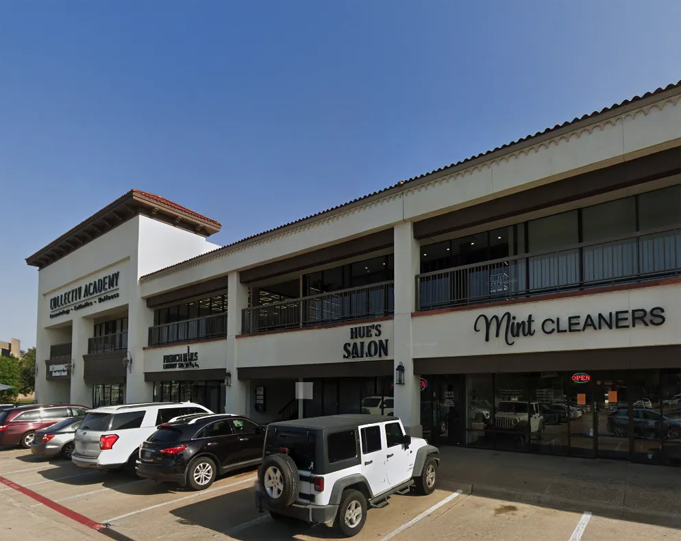 A two-story shopping plaza with businesses including Collectiv Academy, Hue’s Salon, and Mint Cleaners; cars are parked in front of the building.