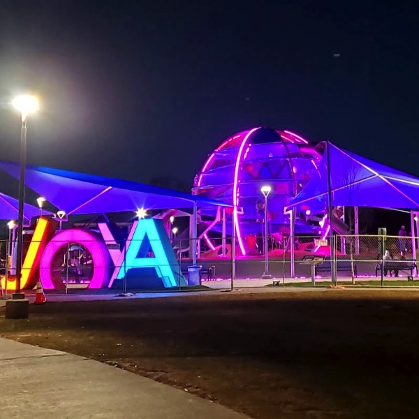 A park at night with large illuminated letters and a domed structure, both lit in pink and purple lights.