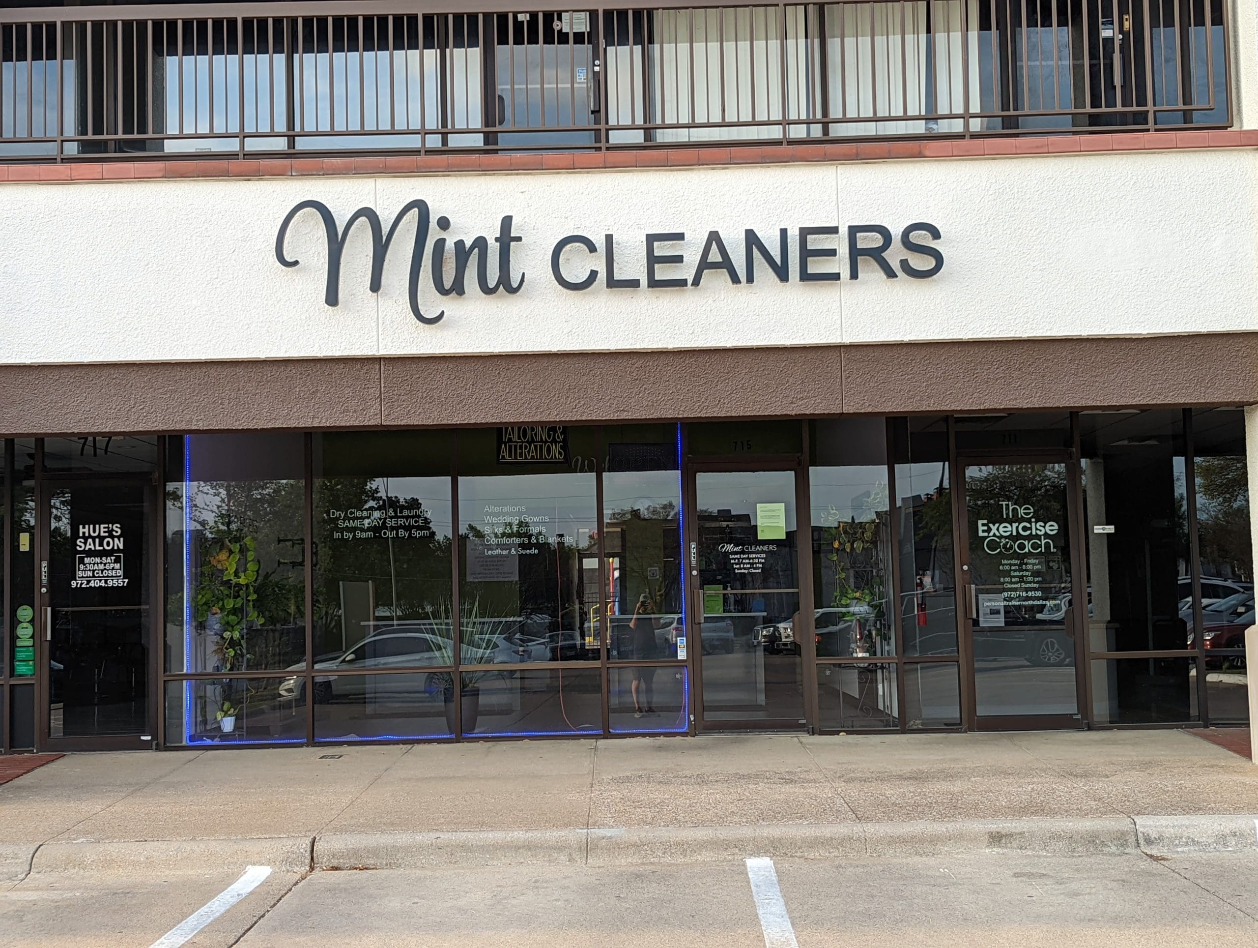 Storefront of Mint Cleaners in a small shopping center, with neighboring businesses Hue’s Salon and The Exercise Coach visible through glass windows.