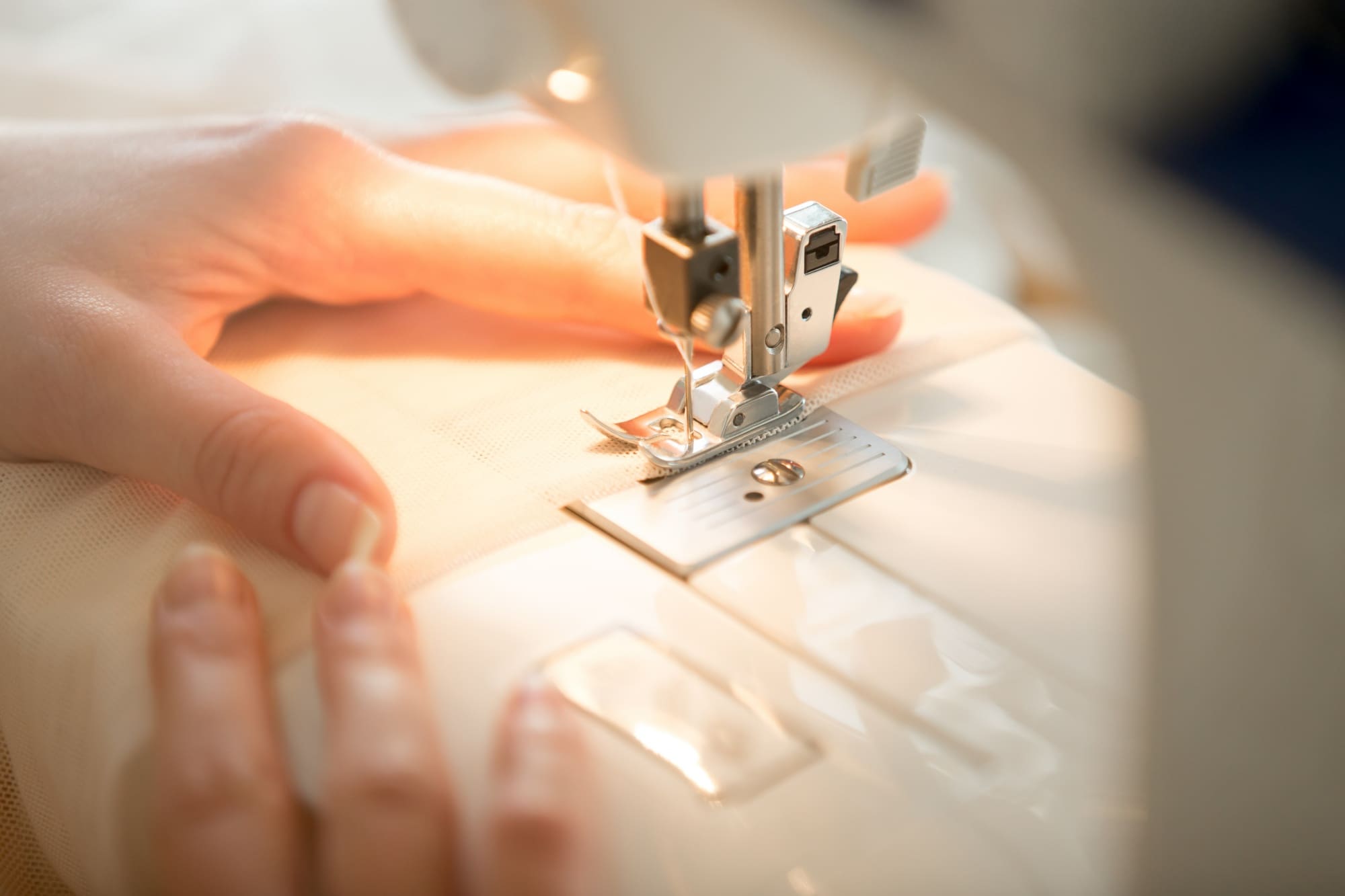 Close-up of a person's hands guiding fabric through a sewing machine while stitching.