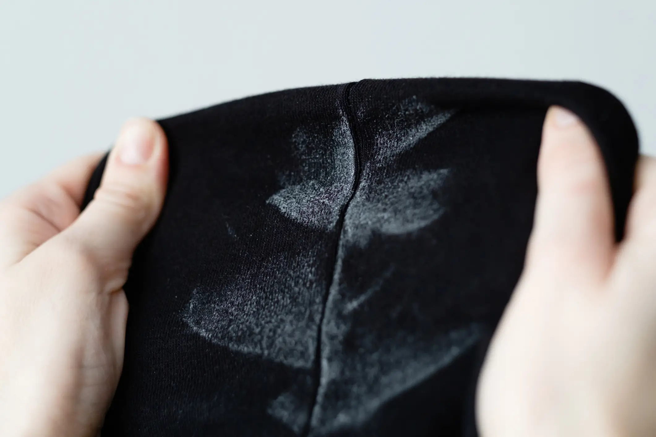 Hands holding a piece of black fabric with visible white deodorant or antiperspirant stains on its surface.